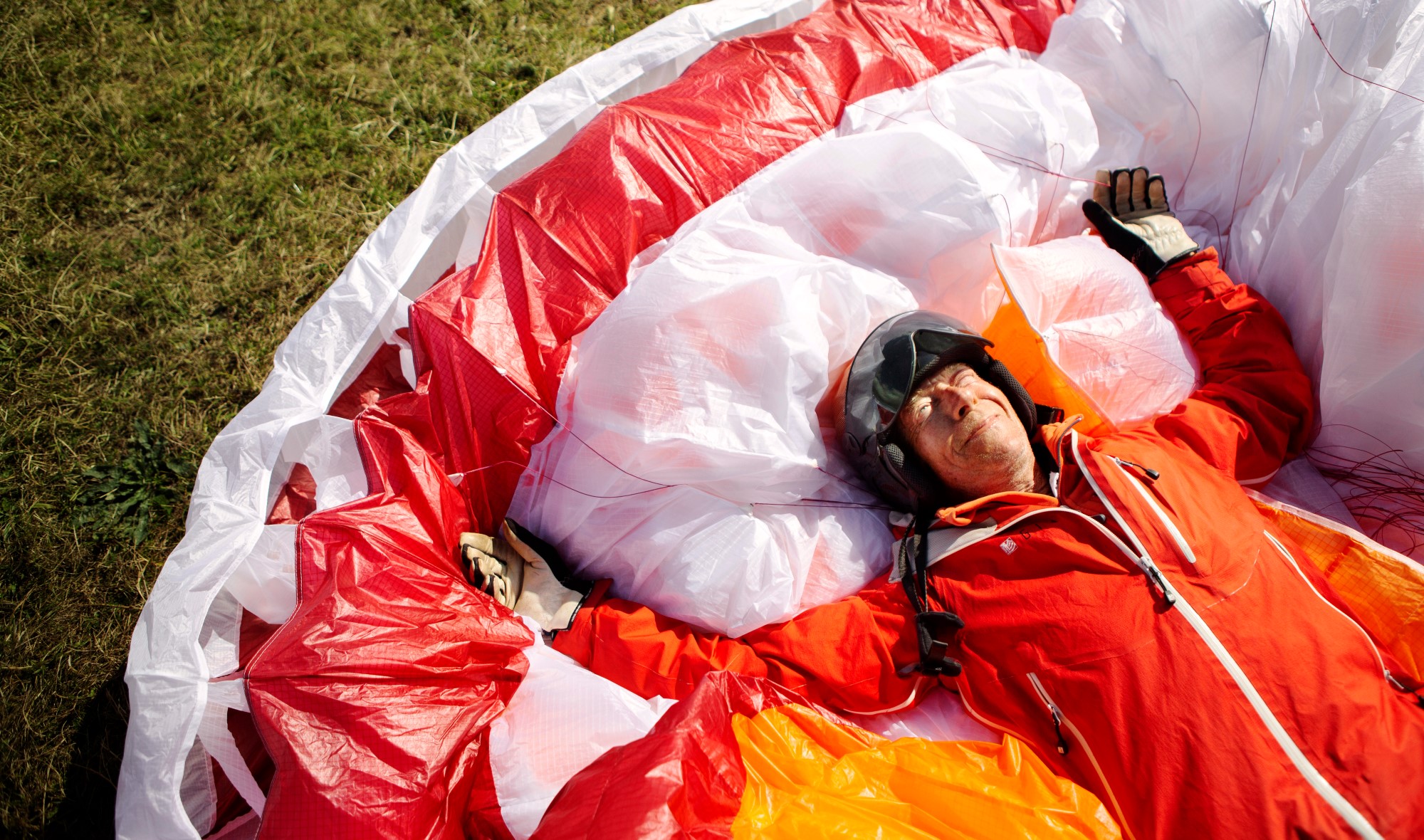 En man ligger i gräset på en fallskärm och ser glad ut.